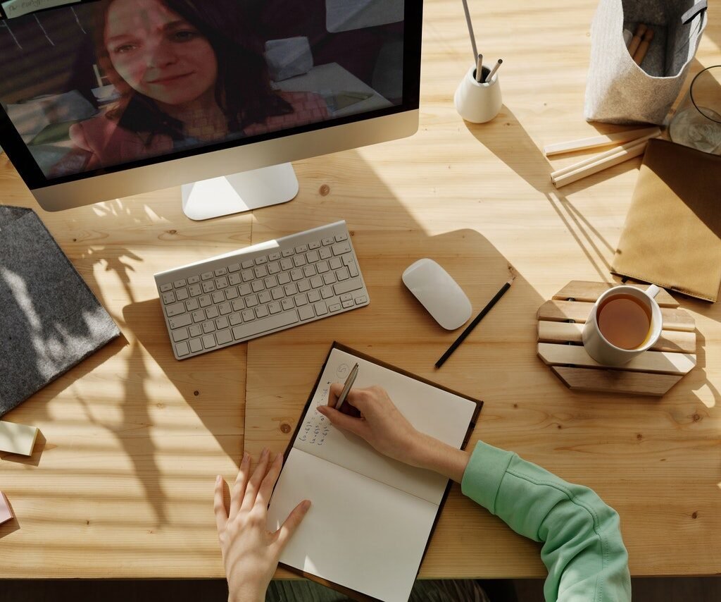 a wooden desk with someone's arm writing in a journal